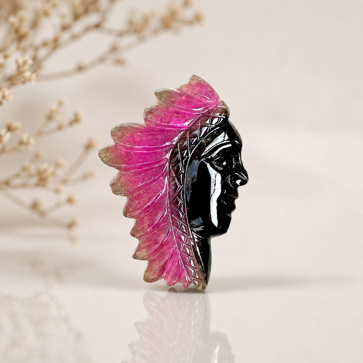 Handcrafted pink and black gemstone chief head carving with detailed feather design displayed on a soft neutral background.